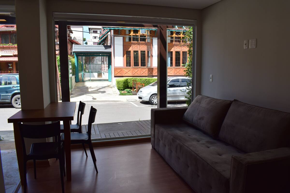 Une pièce avec une table en bois, deux chaises, un canapé et une vue sur une rue animée, avec des voitures et des immeubles.