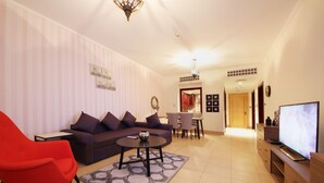 A living room with a sofa, a red chair, a coffee table, a TV, and a dining area with chairs and a table. - Piks Key - Miska 3 (Dubai)