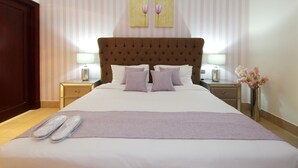 A neatly made bed with pillows and a blanket, a nightstand with a lamp, and a vase with flowers. - Piks Key - Miska 3 (Dubai)