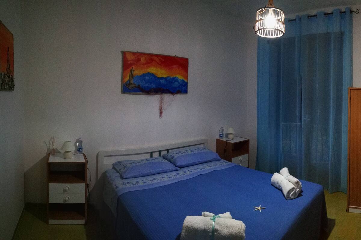 Une chambre à coucher comprenant un lit, une table de chevet, une armoire, un tableau et un luminaire suspendu.