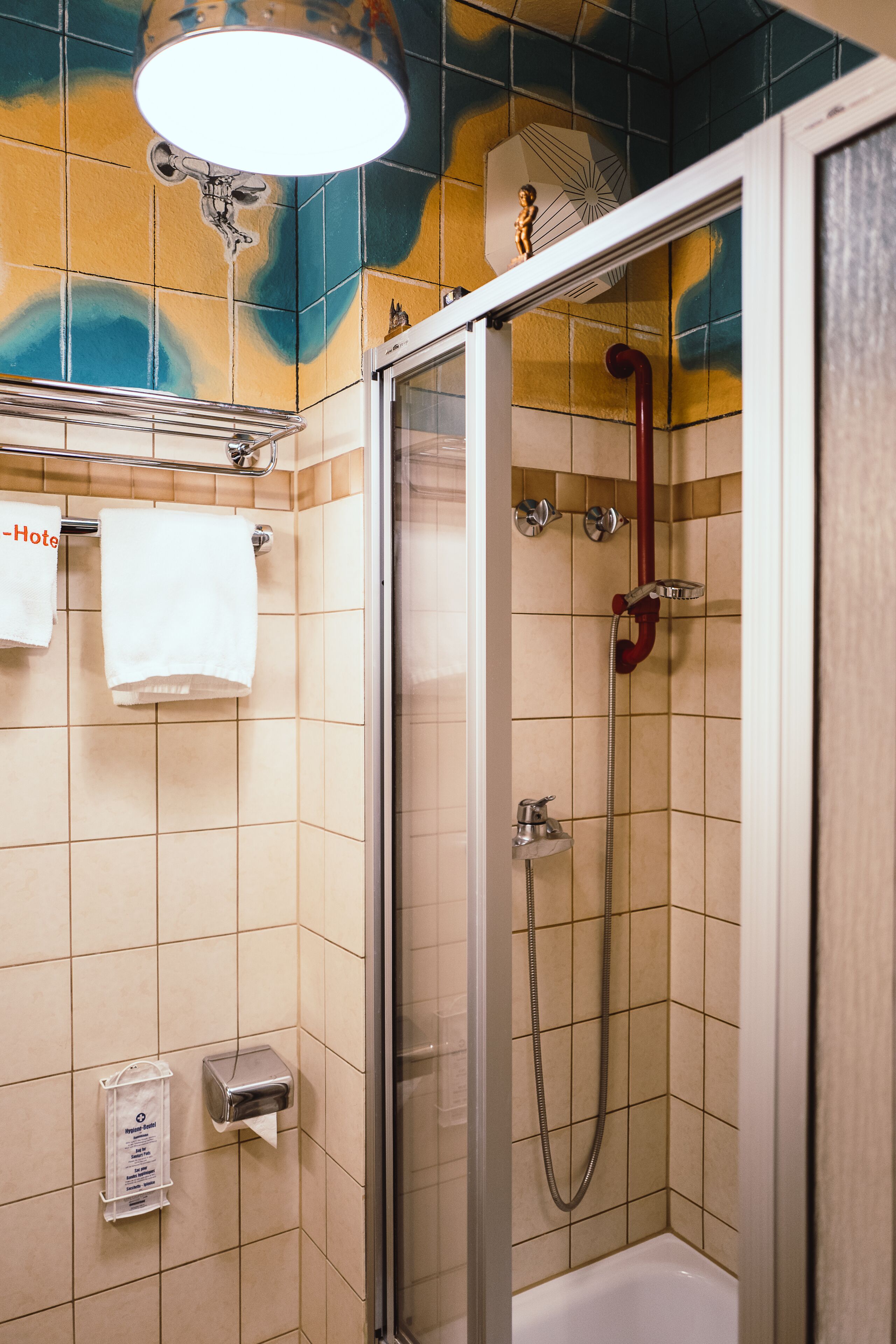 Una ducha con puerta de vidrio, una bañera blanca y un perchero con dos toallas blancas.