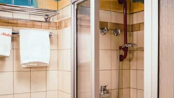 Una ducha con puerta de vidrio, una bañera blanca y un perchero con dos toallas blancas.