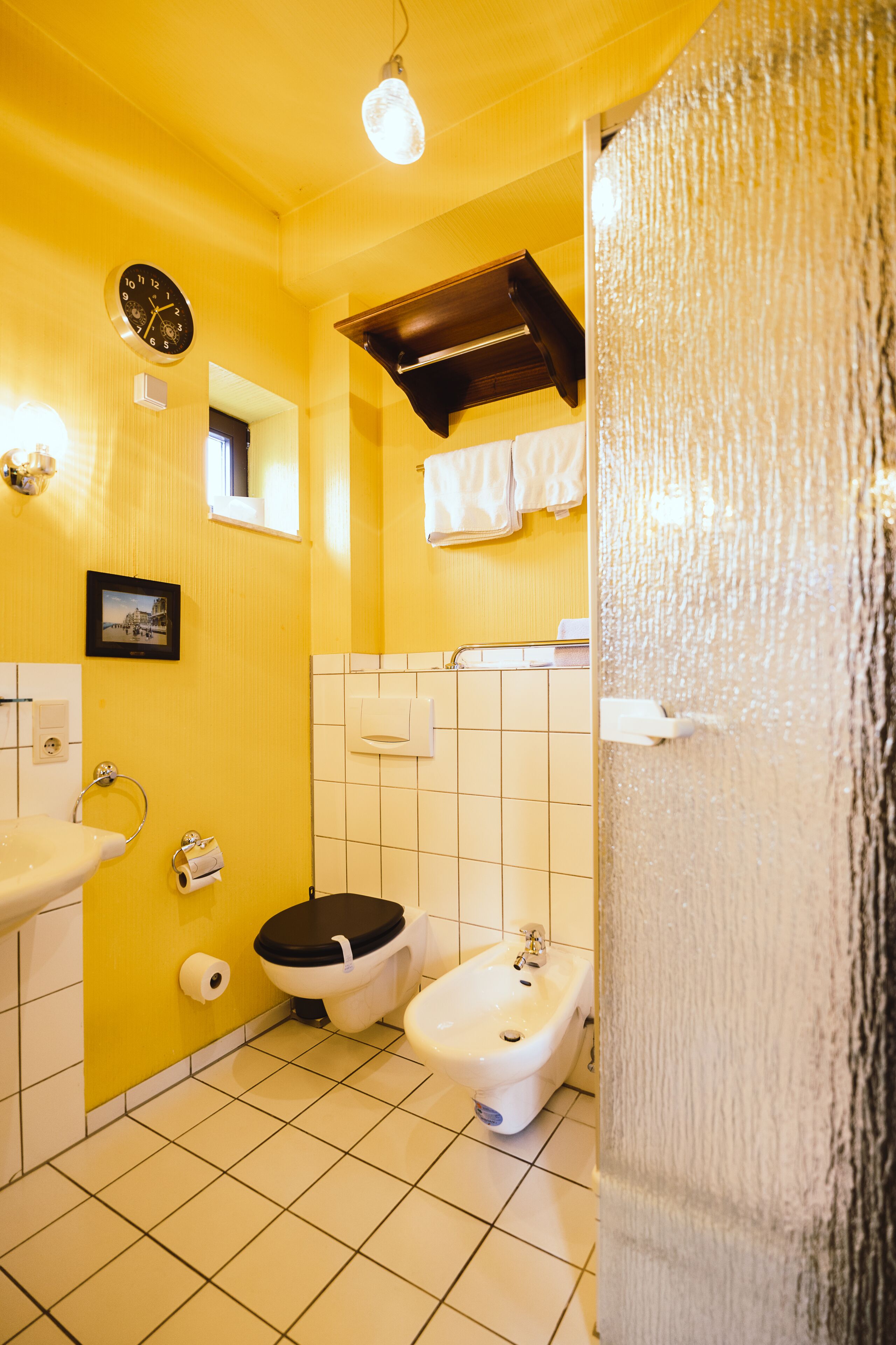 Un baño con paredes amarillas, un lavamanos, un inodoro, un bidé y un espejo.