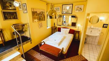 A hotel room with a bed, a bathroom, a staircase, and a wall with framed pictures.