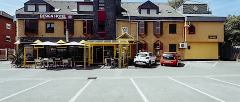 Un hotel con fachada amarilla, un área de estar techada al aire libre y un estacionamiento.