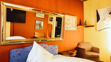 A hotel room with a large bed, a chair, a small table, a mirror, and a chandelier.