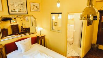 Habitación de hotel con cama, mesita de noche, espejo, lámpara, puerta de baño y suelo estampado.