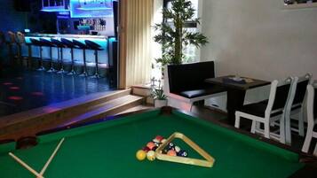 A pool table with billiard balls, a bar area with stools, and a seating area with chairs.