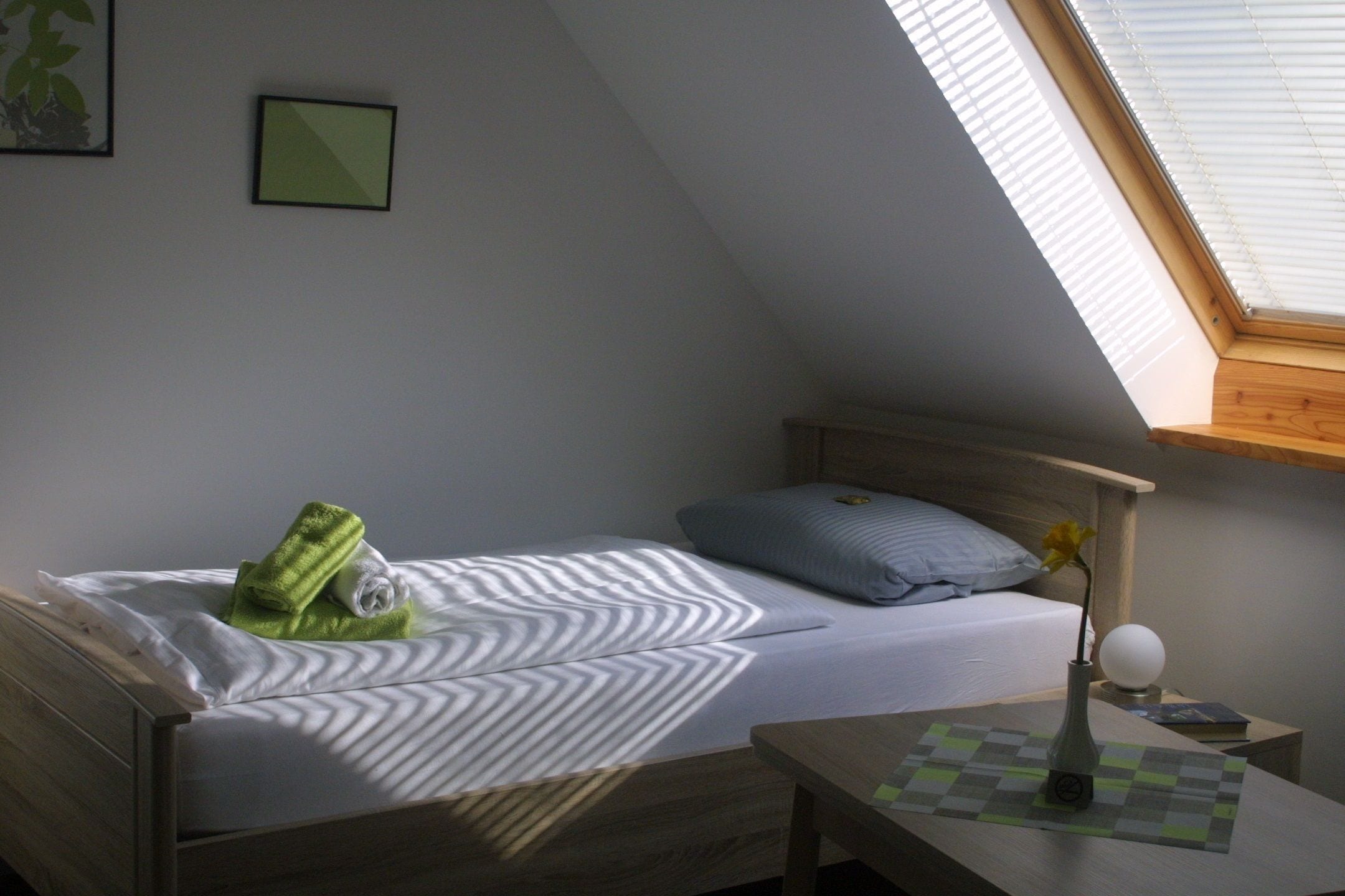 A bedroom with a bed, a nightstand, a vase with a flower, and a skylight.
