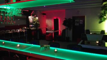 A bar area with a counter, chairs, and tables. There is a plant and a clock on the wall.