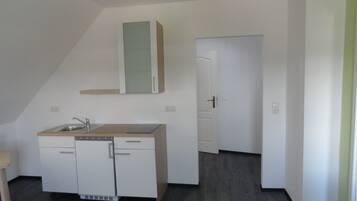 A small, modern kitchen with white cabinets, a sink, and a countertop. There is a door leading to another room.