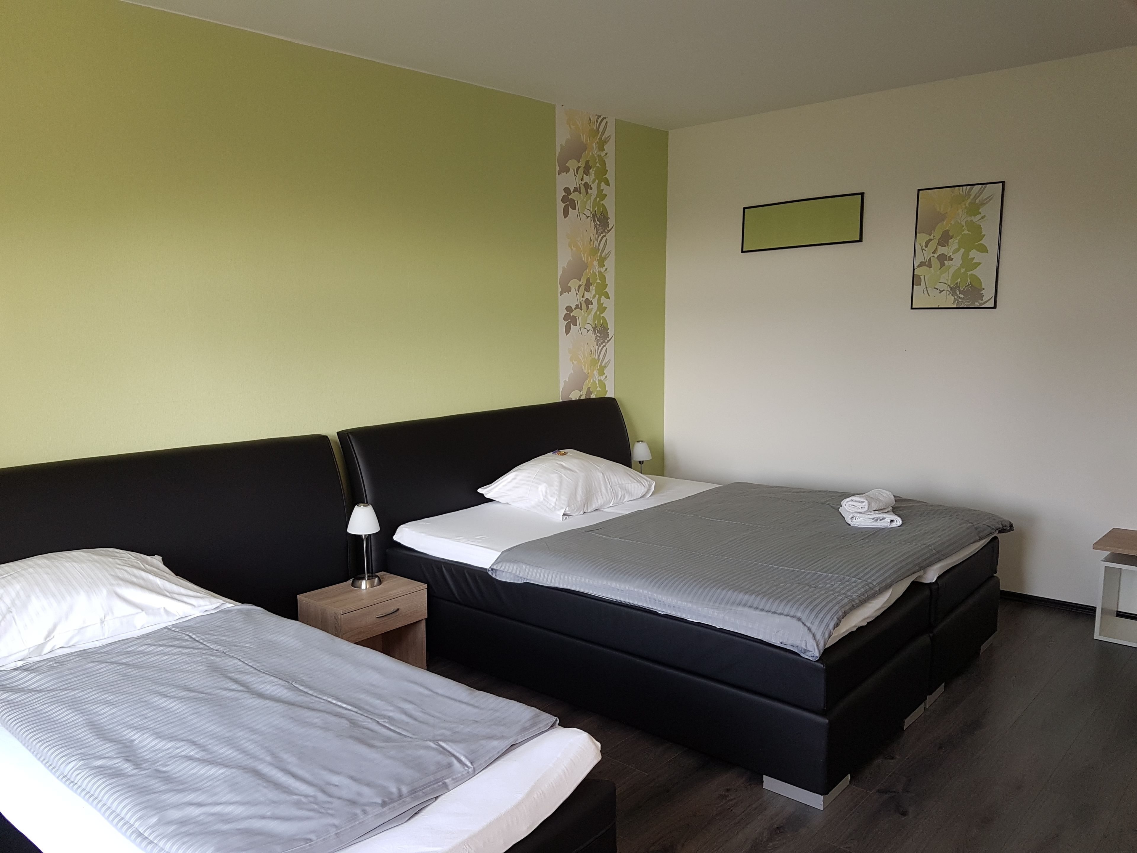 A hotel room with two beds, a nightstand, a lamp, and two framed pictures on the wall.