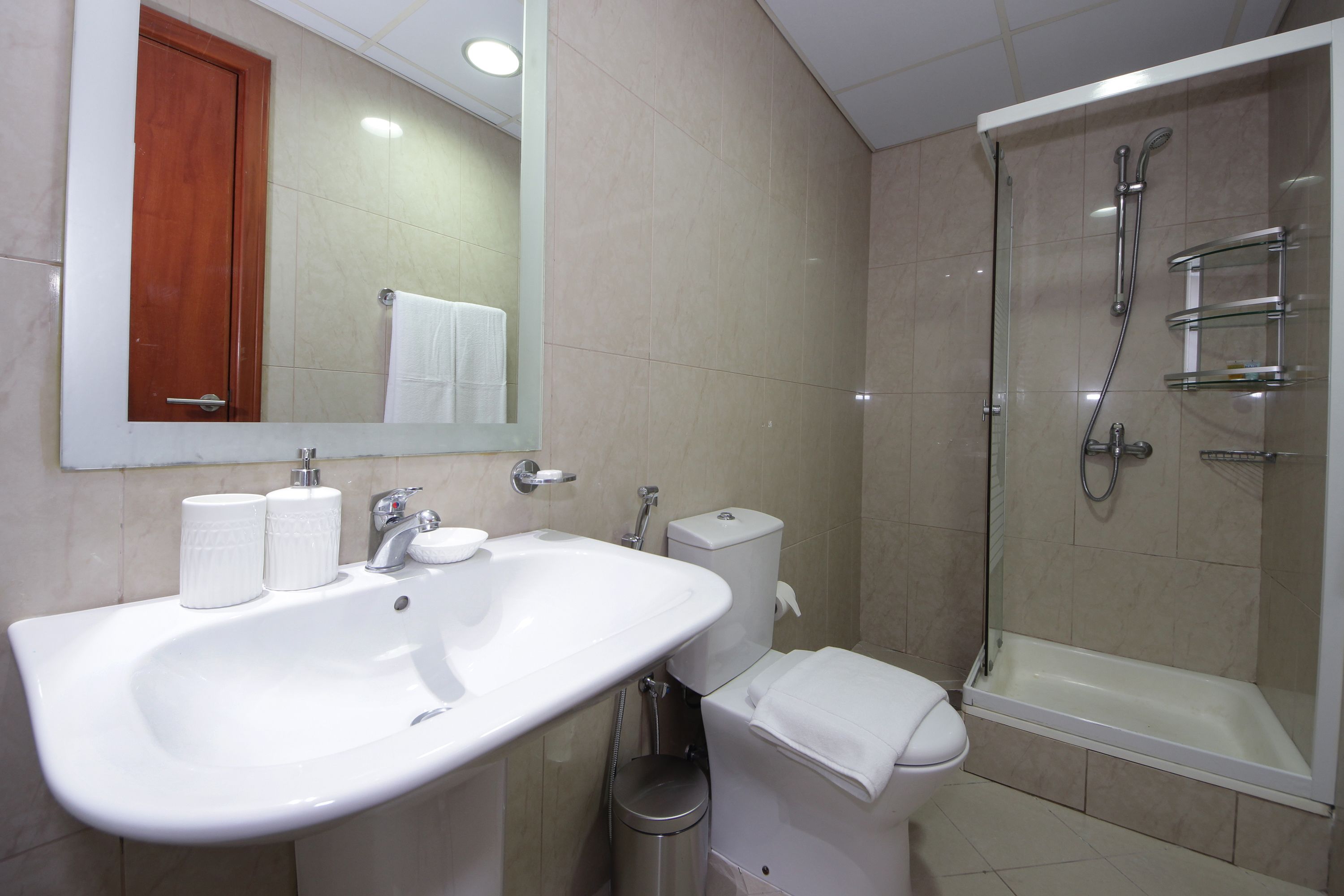 A bathroom with a white sink, mirror, toilet, and glass-enclosed shower.