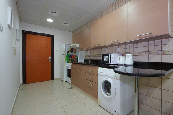 A compact kitchen with a washing machine, microwave, and a small refrigerator.