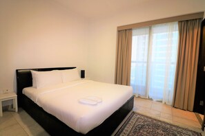 Ein Hotelzimmer mit einem großen Bett, einem Nachttisch, einem Fenster mit Vorhängen und einem gemusterten Teppich.
