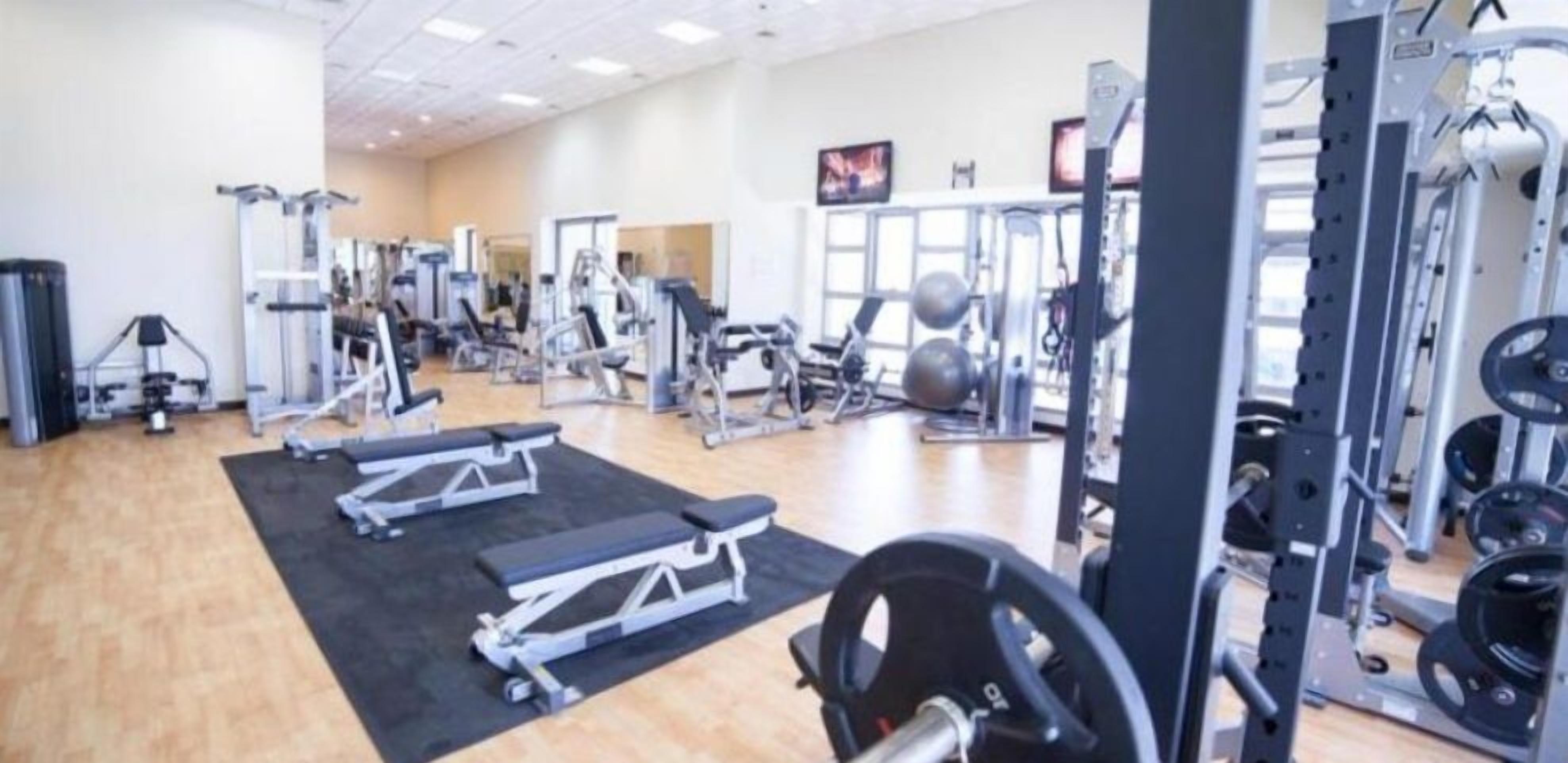 Un gimnasio con diverso equipo de ejercicio, incluyendo bancos, máquinas de pesas y pesas libres.