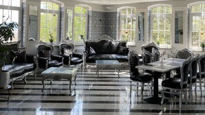 Una habitación amplia con suelo a rayas blanco y negro, ventanas grandes y muebles clásicos.