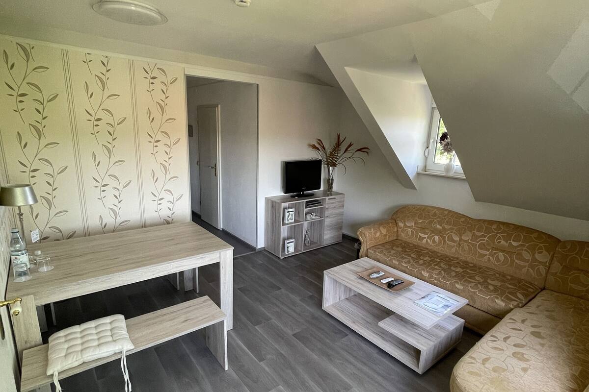 Una sala de estar moderna con un sofá, una mesa de centro, televisor y un comedor con banco y mesa.