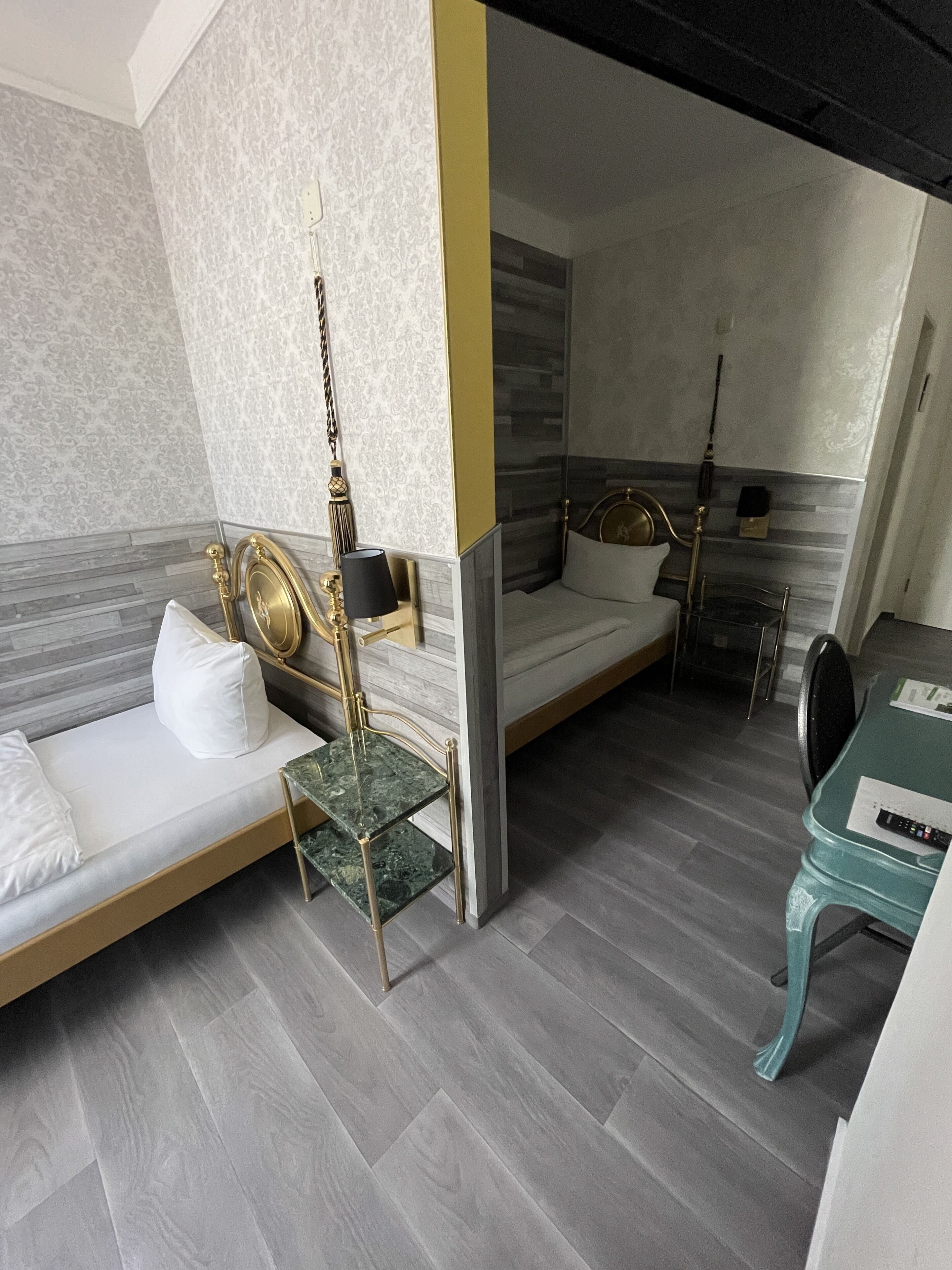 A modern hotel room with two beds, a marble-topped table, and a green chair.