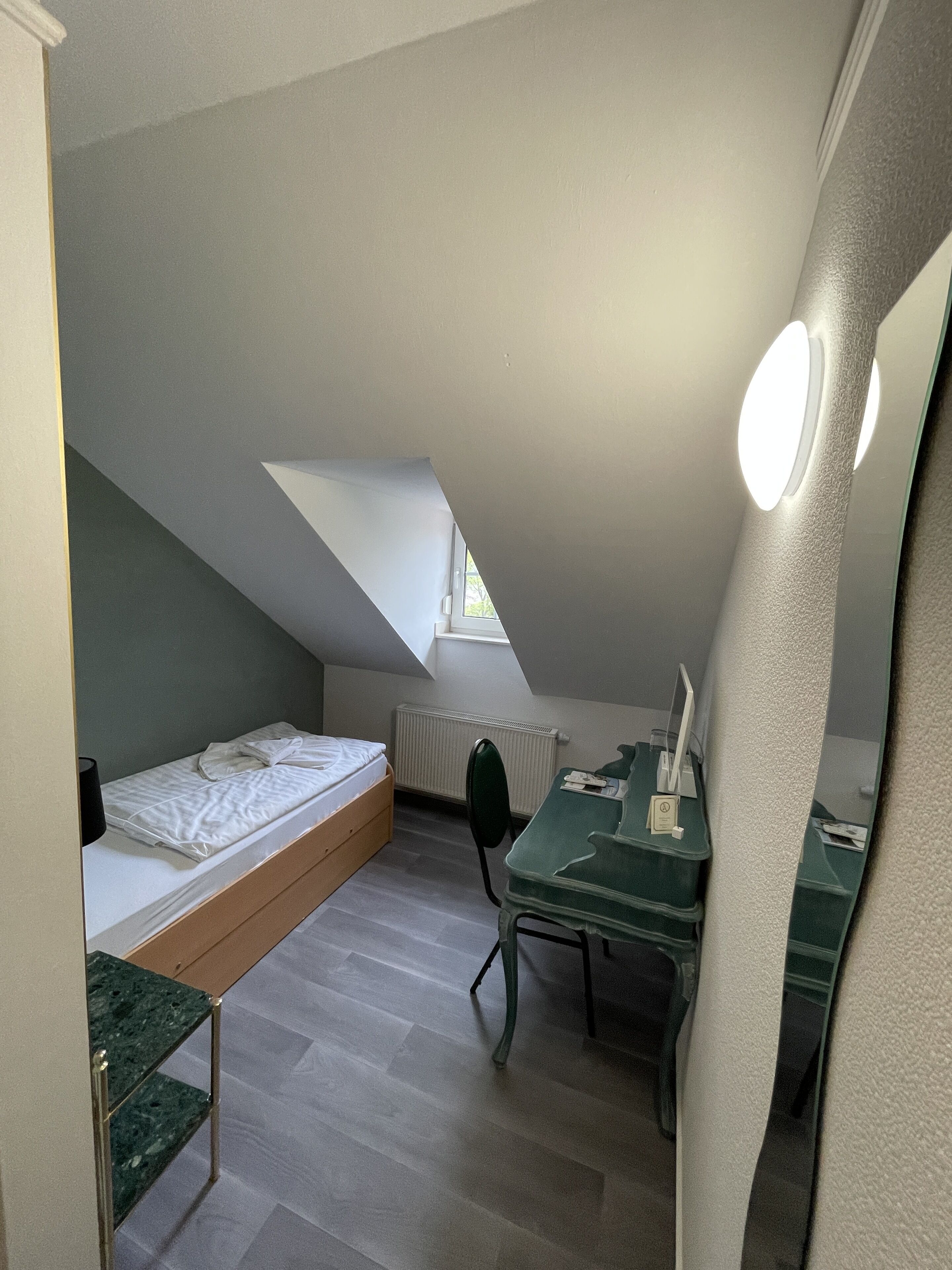 A small, compact room with a sloped ceiling, a bed, a desk, and a chair.