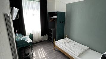 Habitación de hotel compacta con una cama individual, un escritorio con silla, un armario y una mesita.