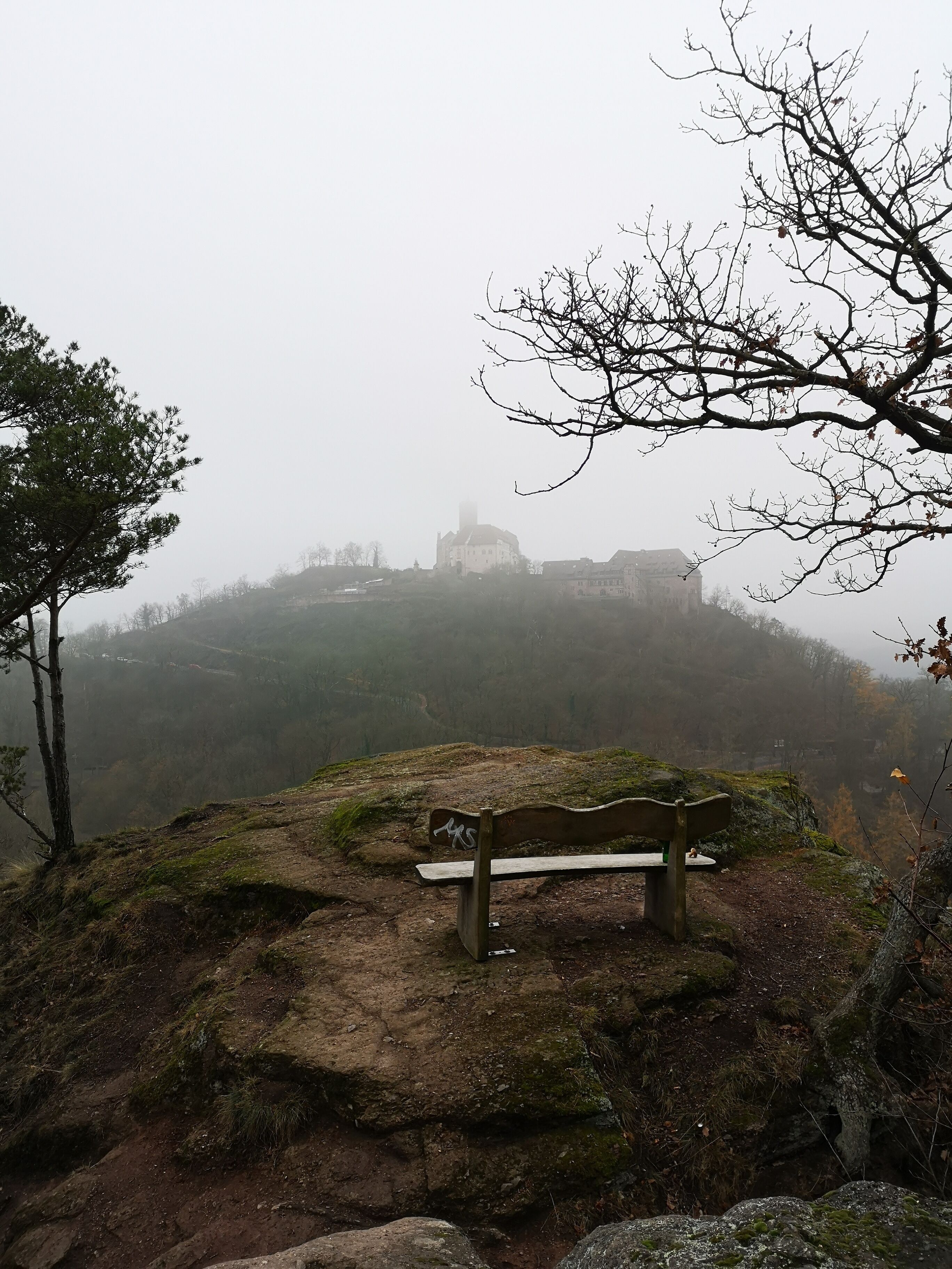 Un banco sobre un promontorio rocoso con vistas a un paisaje brumoso y un edificio a lo lejos.