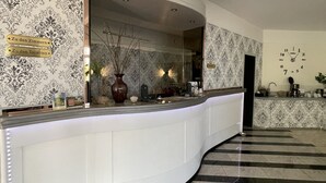 Zona de recepción de un hotel con un mostrador blanco curvo, un reloj en la pared y un diseño de papel tapiz estampado.