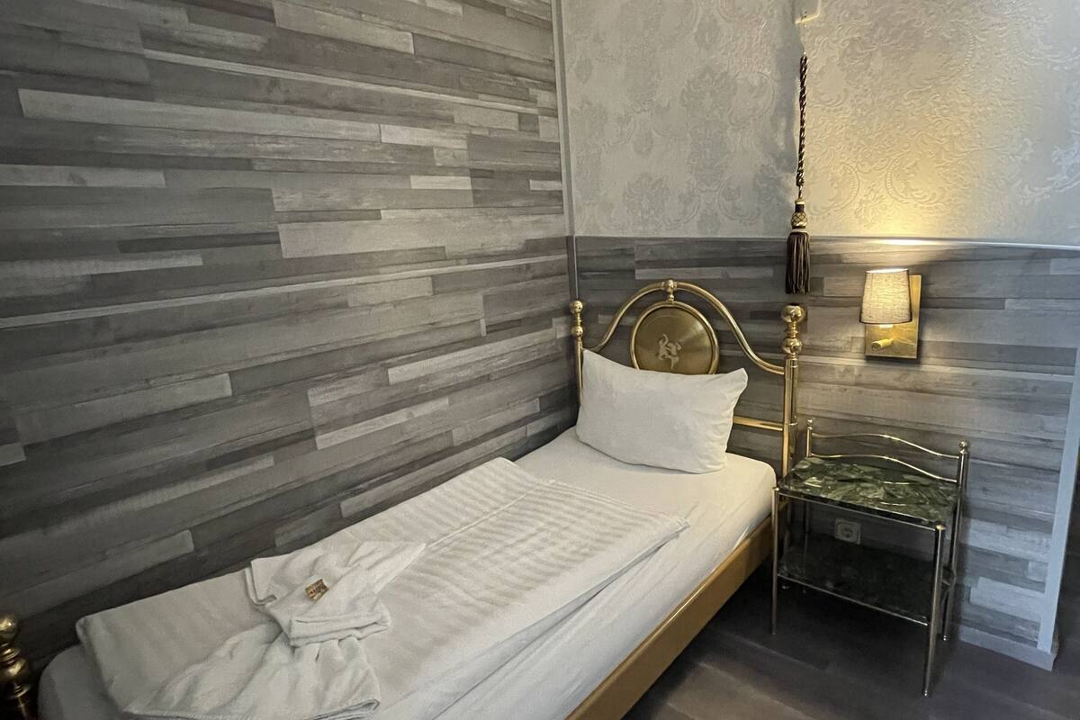 Una cama bien tendida con un cabecero, una mesita de noche con una lámpara y una pared con textura.