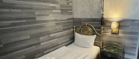 A neatly made bed with a headboard, a bedside table with a lamp, and a wall with a textured pattern.
