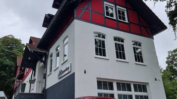 A two-story building with a red and white facade, a visible sign reading "Kaufhaus," and a red vintage car parked in front.