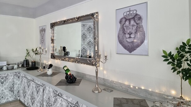 Un baño con un espejo grande, una obra de arte con león enmarco y un candelabro decorativo.