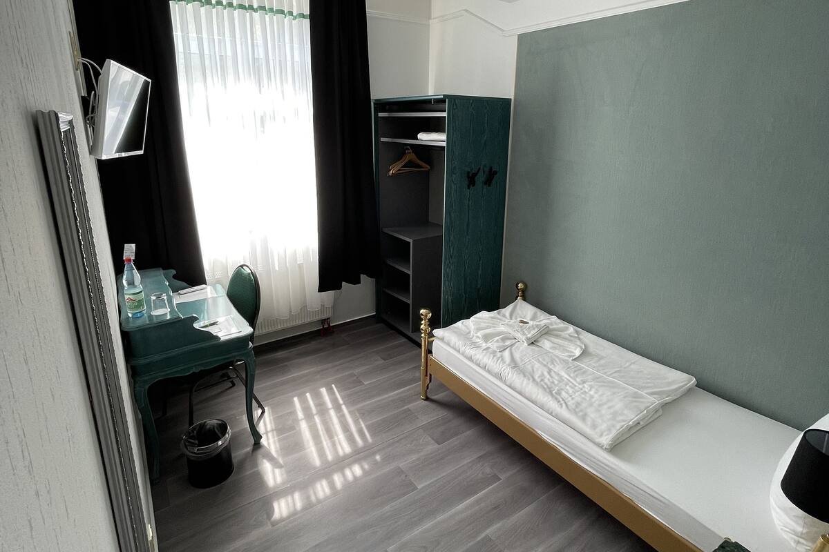 Una habitación con cama, escritorio, silla, armario y espejo.