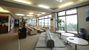 A spacious lounge area with a sofa, round tables, and a reception desk. - HOTEL Akenohoshi (Muroto)