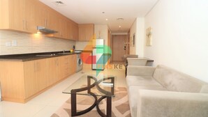 Una cocina moderna con armarios de madera, una mesa con cubierta de vidrio y un sofá beige en la sala de estar.