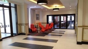 Vestíbulo de hotel con piso a cuadros, sillas rojas y una escalera que conduce a otra zona.