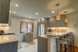 A modern kitchen with grey cabinetry, a central island with bar stools, a stainless steel refrigerator, and pendant lighting. - 732b Meadow Creek 2 Bedroom Townhouse by RedAwning (Frisco)
