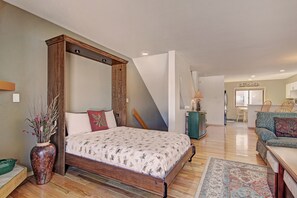 A bedroom with a four-poster bed, a wooden floor, a green vase with dried plants, and a dining area with a table and chairs.