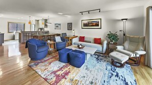 A modern living room with a sofa, chairs, a coffee table, and a dining area with a kitchen in the background. - 732b Meadow Creek 2 Bedroom Townhouse by RedAwning (Frisco)