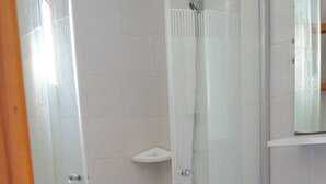 Ducha de esquina con puerta de cristal, lavabo blanco con espejo encima y un tapete morado en el suelo.