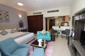 A modern hotel room with a bed, a sofa, a coffee table, a TV, and a kitchenette. - Piks Key - Cricket Tower Sports City (Dubai)