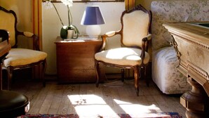 Una stanza con un'ampia finestra, un tavolo di legno con una lampada, due sedie, un divano e un tappeto decorato.