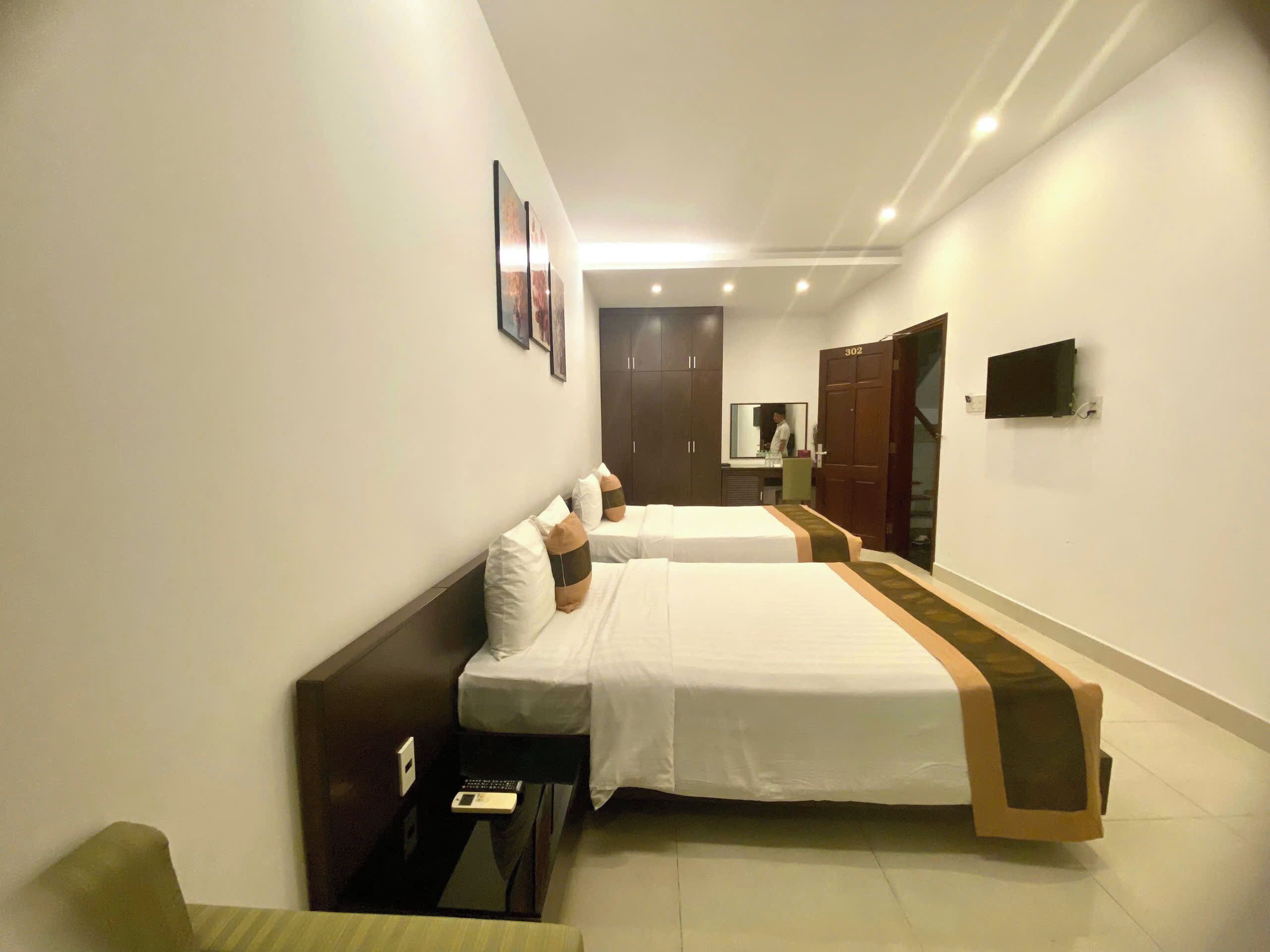 A hotel room with two beds, a desk, a mirror, and a TV.