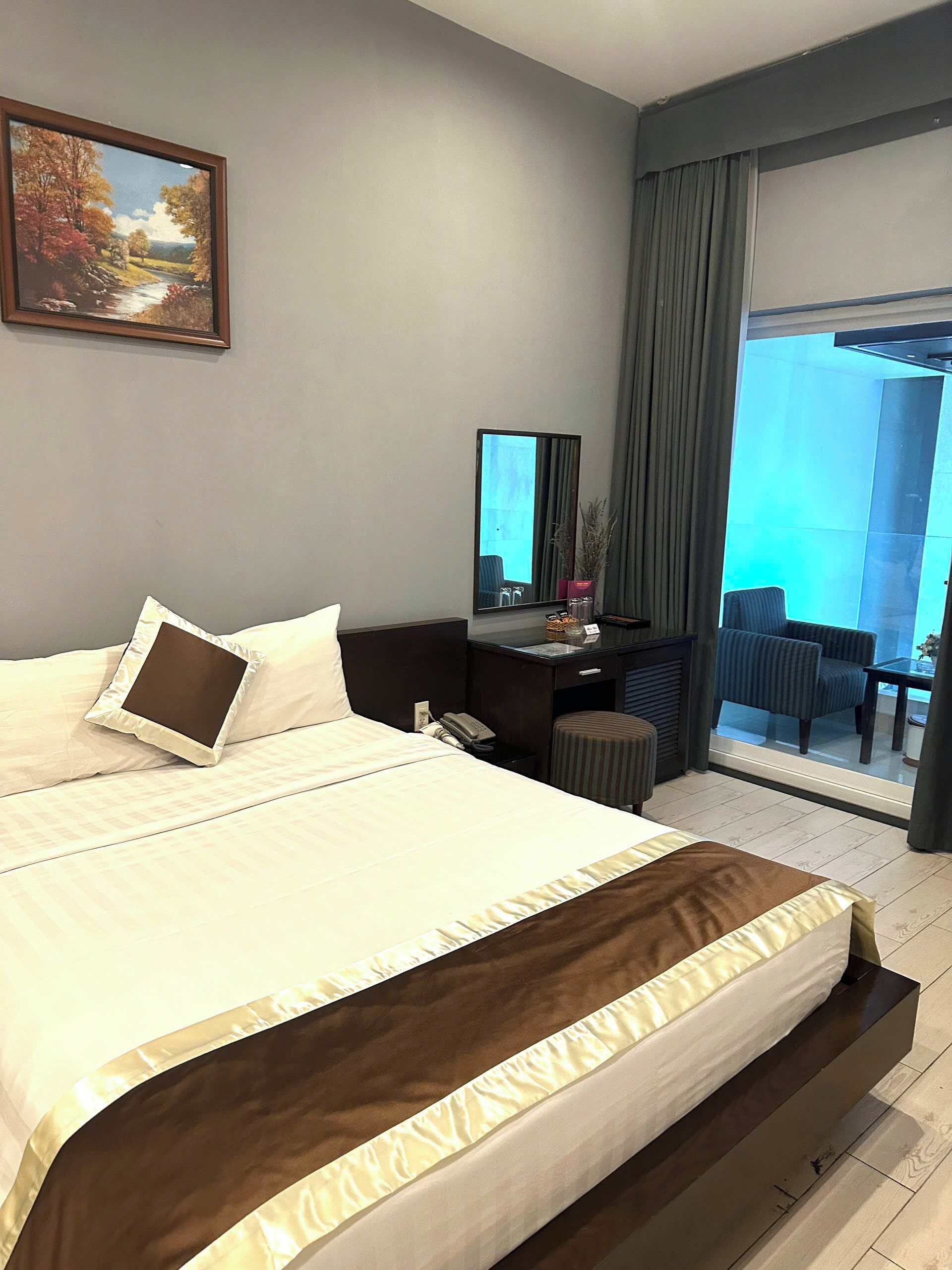 A modern hotel room with a large bed, a desk with a mirror, a chair, and a view of the outdoors.