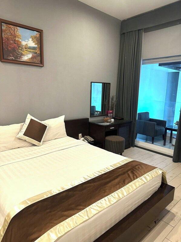 A modern hotel room with a large bed, a desk with a mirror, a chair, and a view of the outdoors.