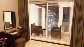 A hotel room with a large sliding glass door leading to a balcony, a desk with a telephone, a chair, and a small ottoman. - Ngoc Linh Luxury Hotel (Ho Chi Minh City)