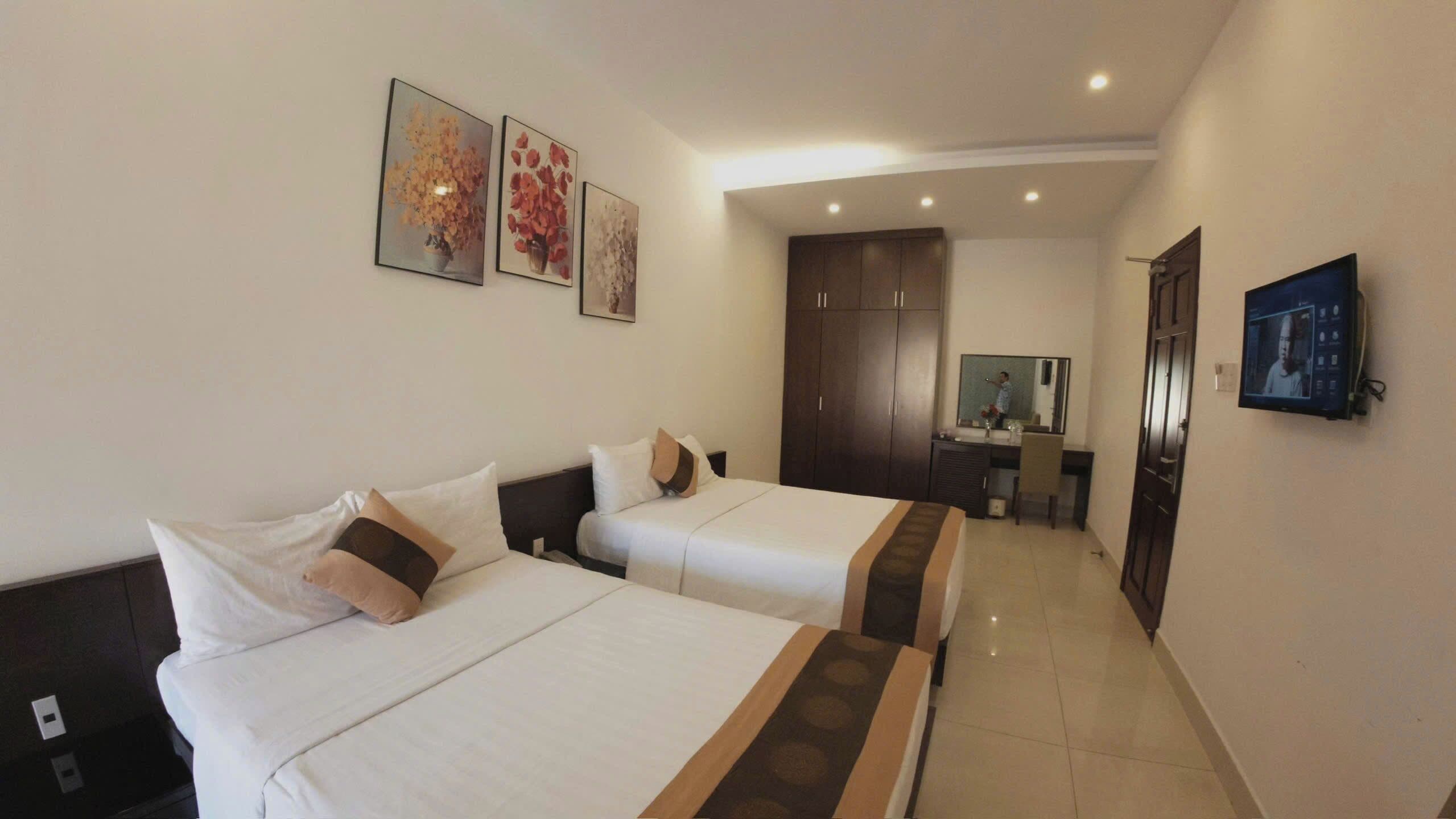A hotel room with two beds, a desk with a chair, a mirror, and a TV.
