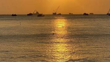 A sunset over a calm sea with several ships and cranes in the distance.