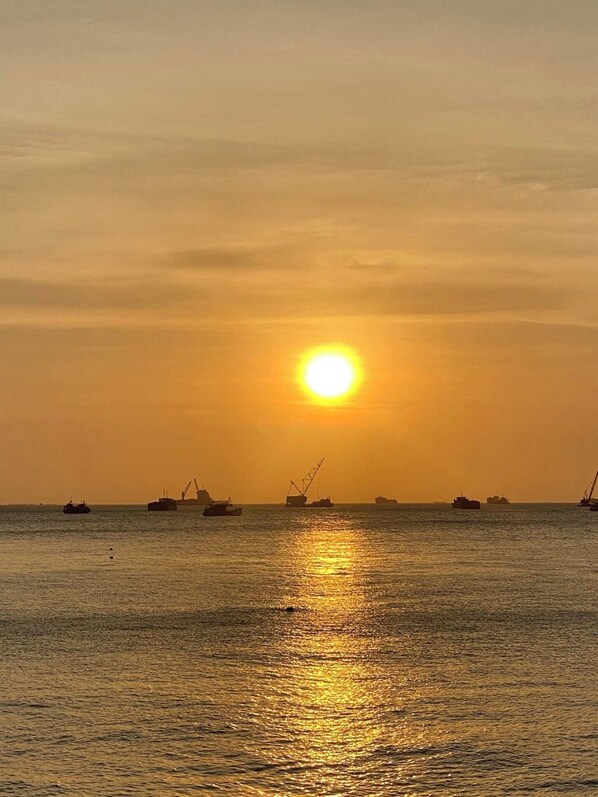 A sunset over a calm sea with several ships and cranes in the distance. - Ngoc Linh Luxury Hotel (Ho Chi Minh City)