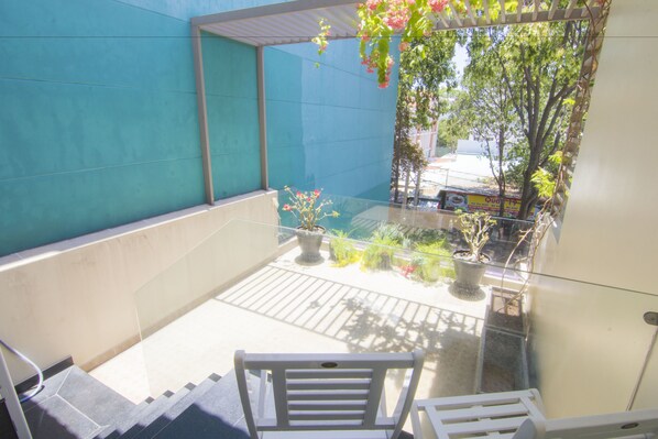 Un balcon doté d’une balustrade en verre, de plantes en pot et d’une chaise blanche.