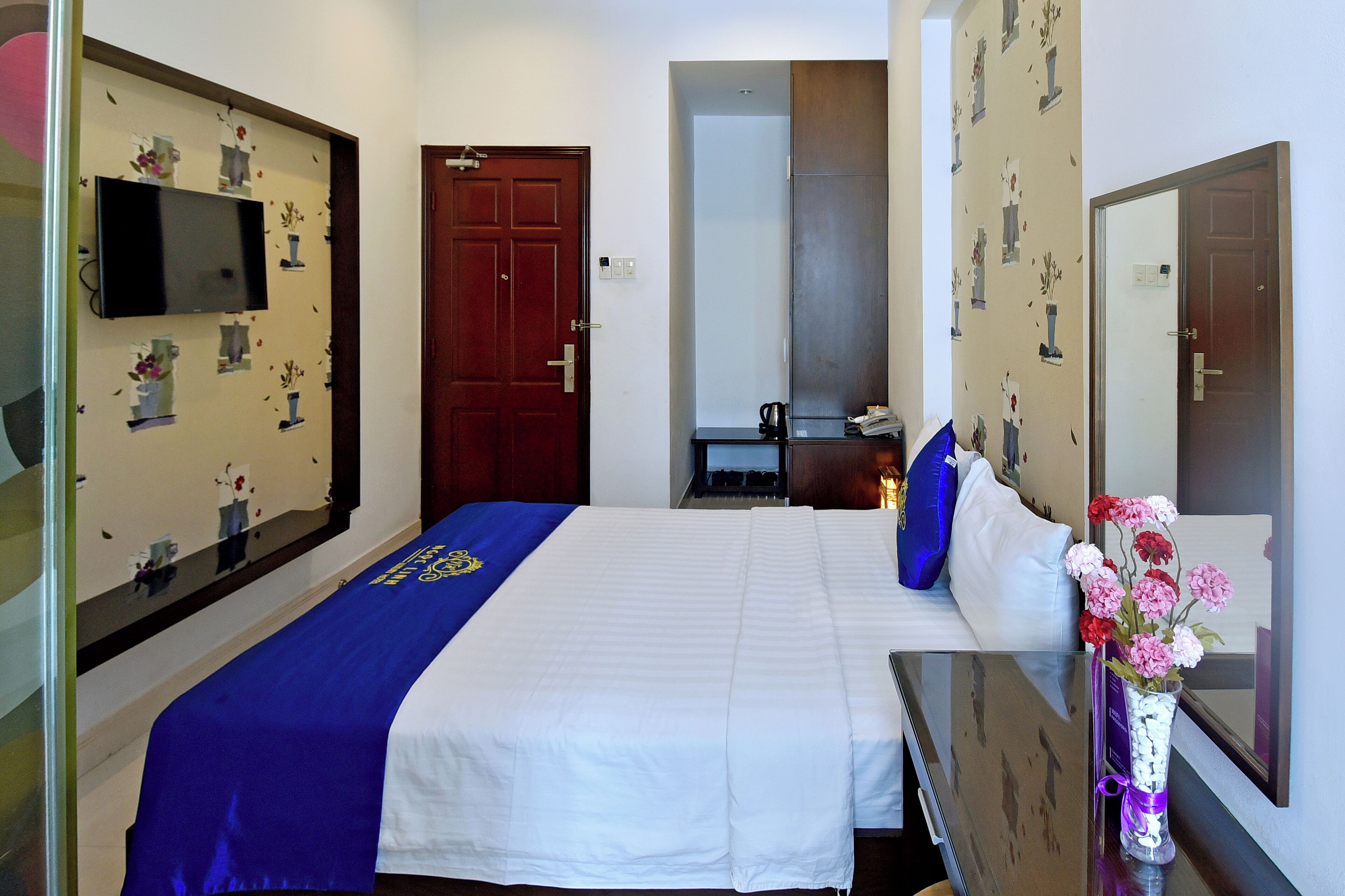 A hotel room with a bed, a TV mounted on the wall, a desk with a chair, and a mirror.